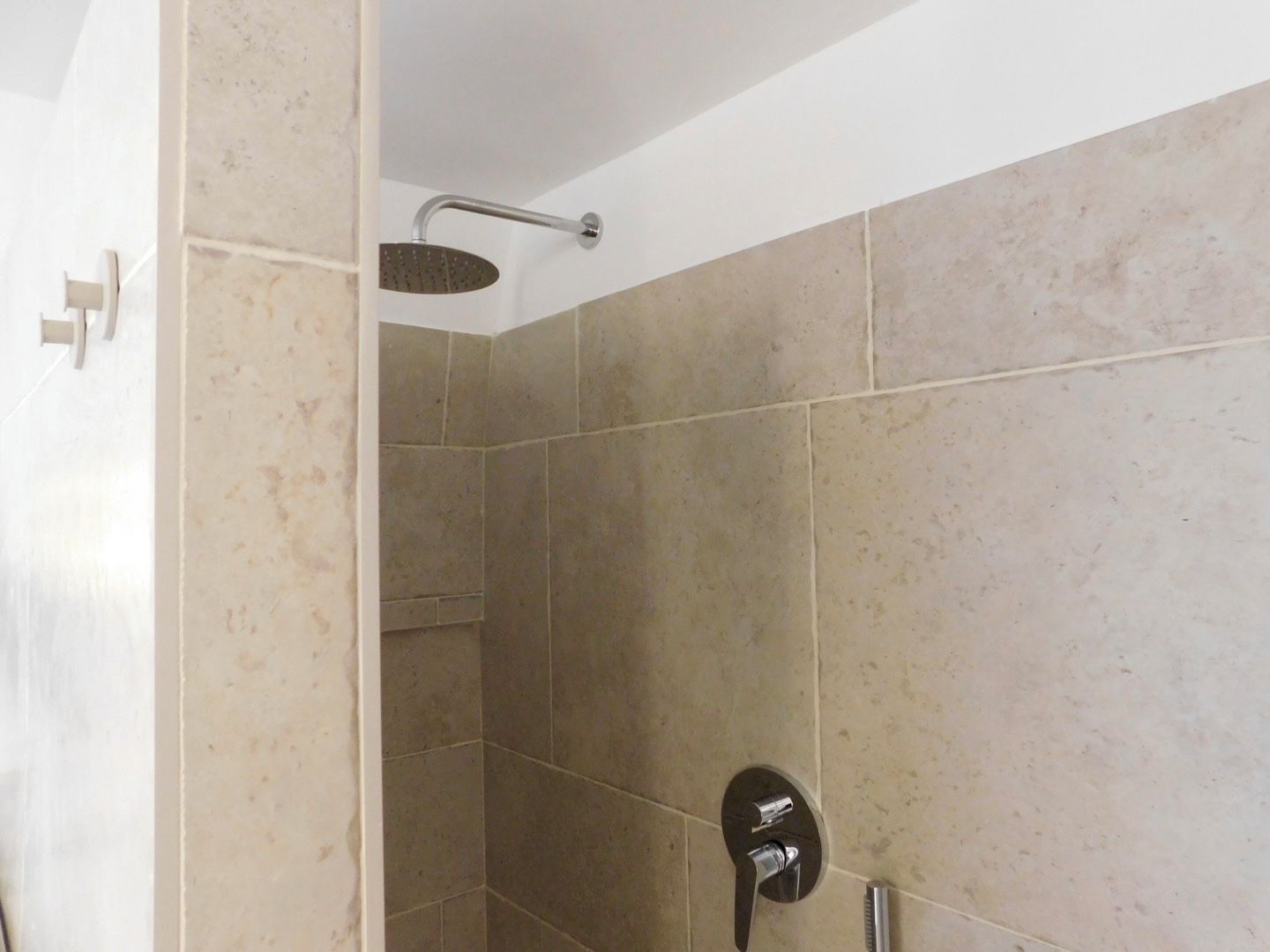 A shower area with a handheld showerhead and a wall-mounted faucet.