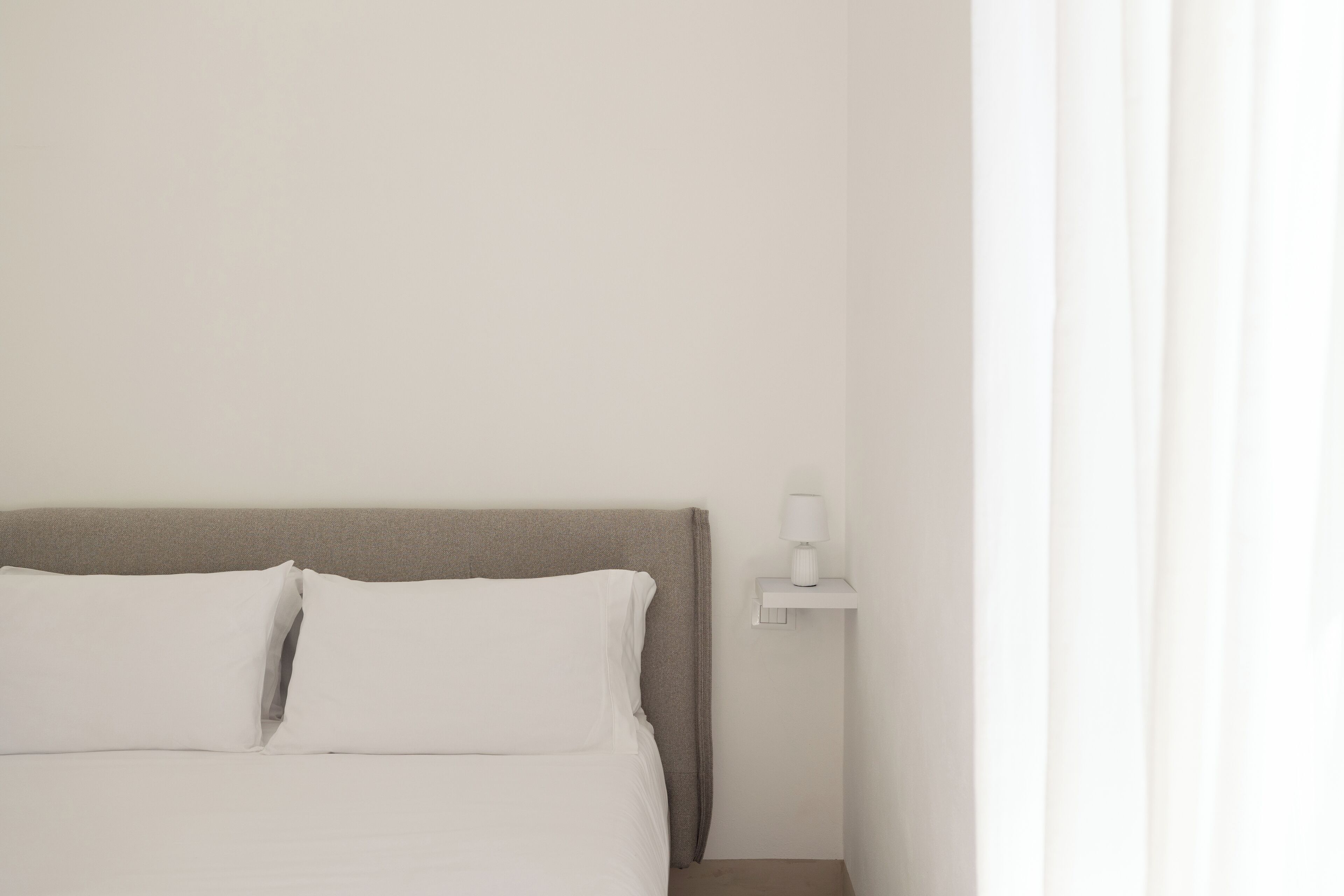 A neatly made bed with white bedding and a grey headboard.