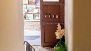 A hallway with a wooden door, a green vase with pampas grass, and framed pictures on the wall.
