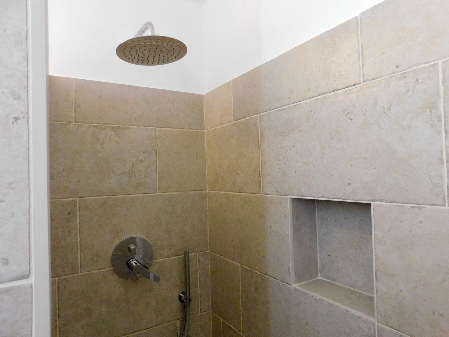 A shower area with a handheld showerhead and a wall-mounted control valve.