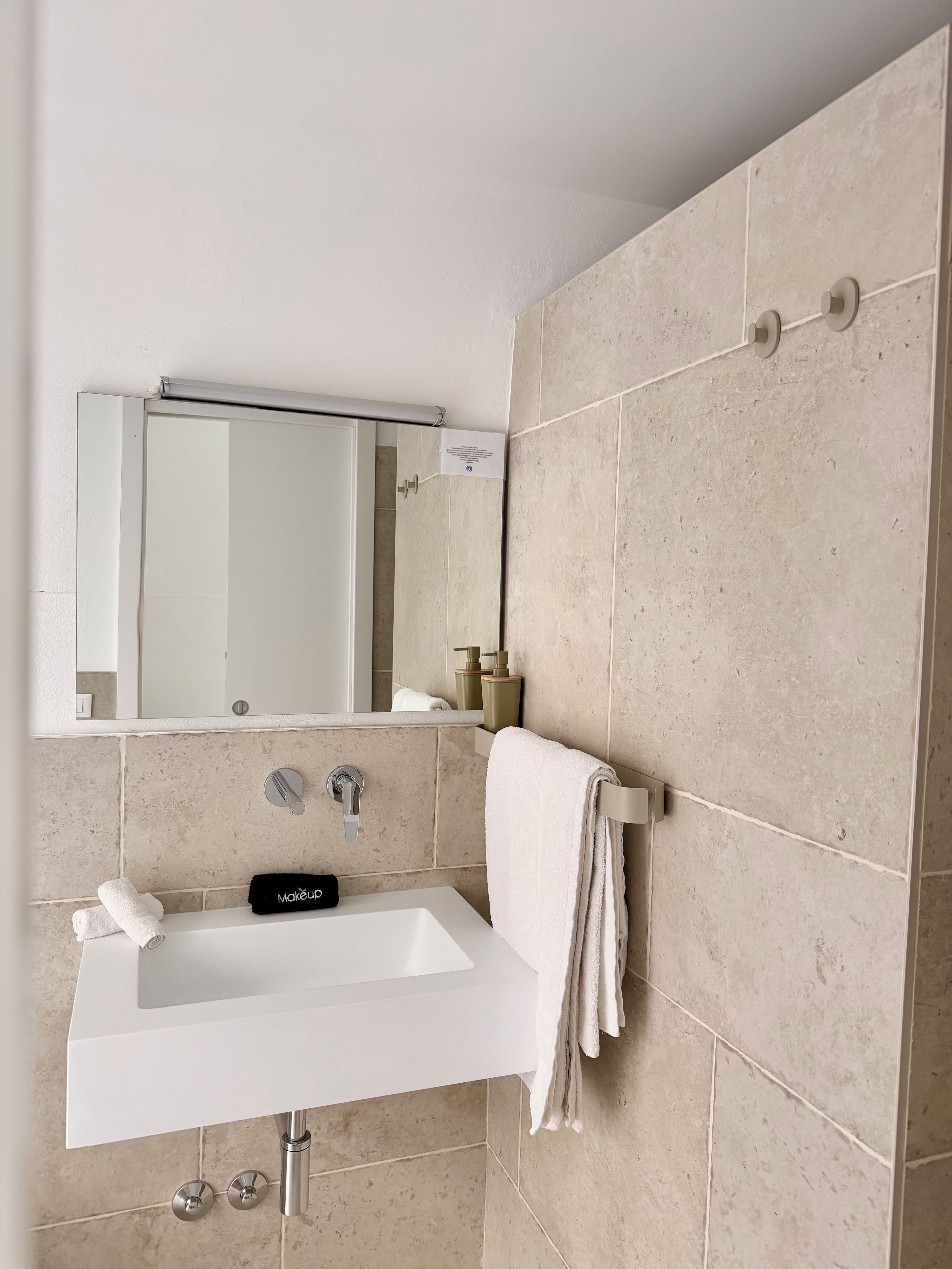 Un baño con un lavamanos blanco, un espejo y baldosas color crema.