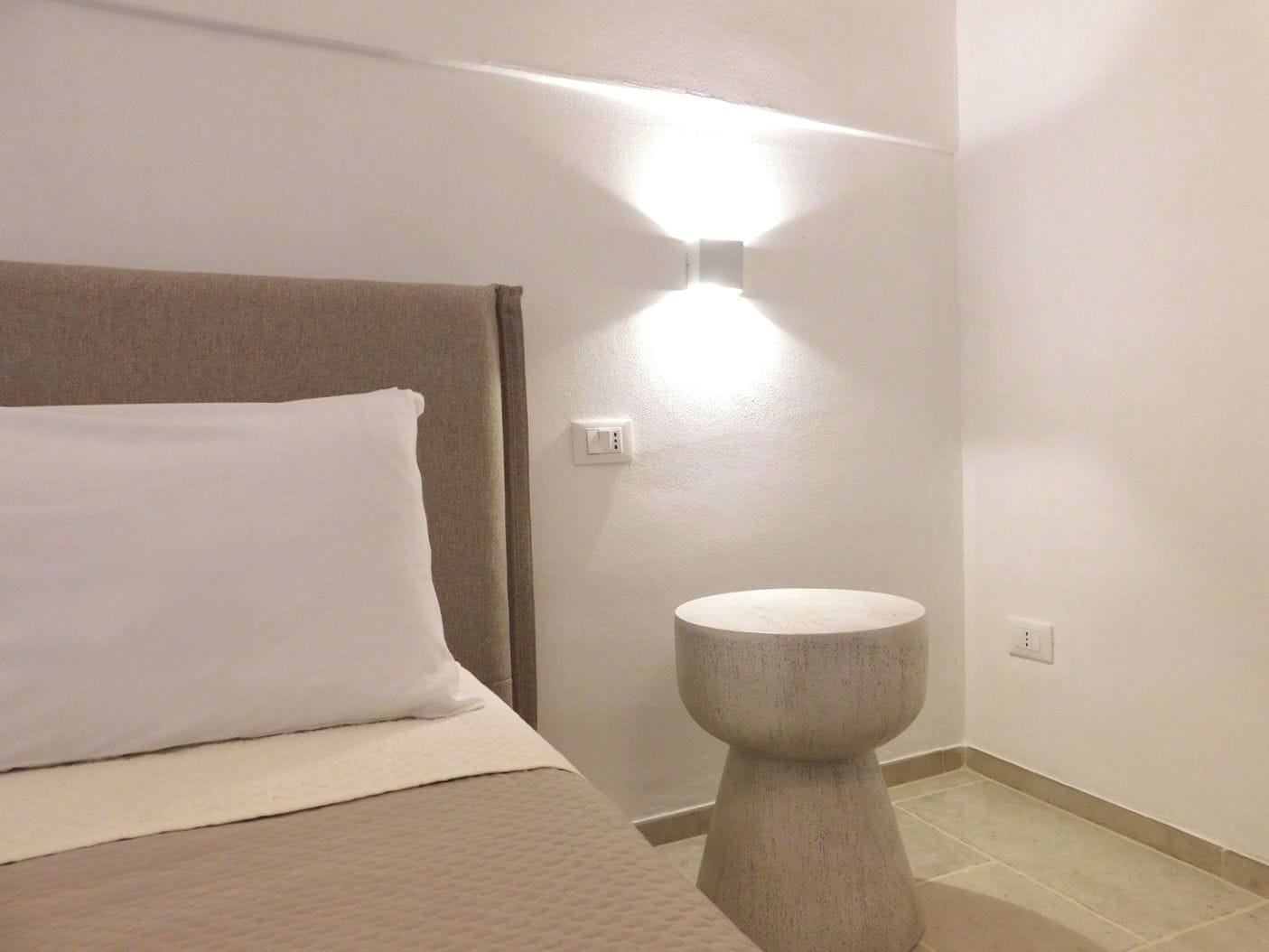 Une chambre d’hôtel avec un lit, un luminaire fixé au mur et une petite table ronde.