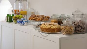 Ein reichhaltiges Frühstücksbuffet mit verschiedenen Backwaren, Früchten und Getränken auf einer weißen Theke.