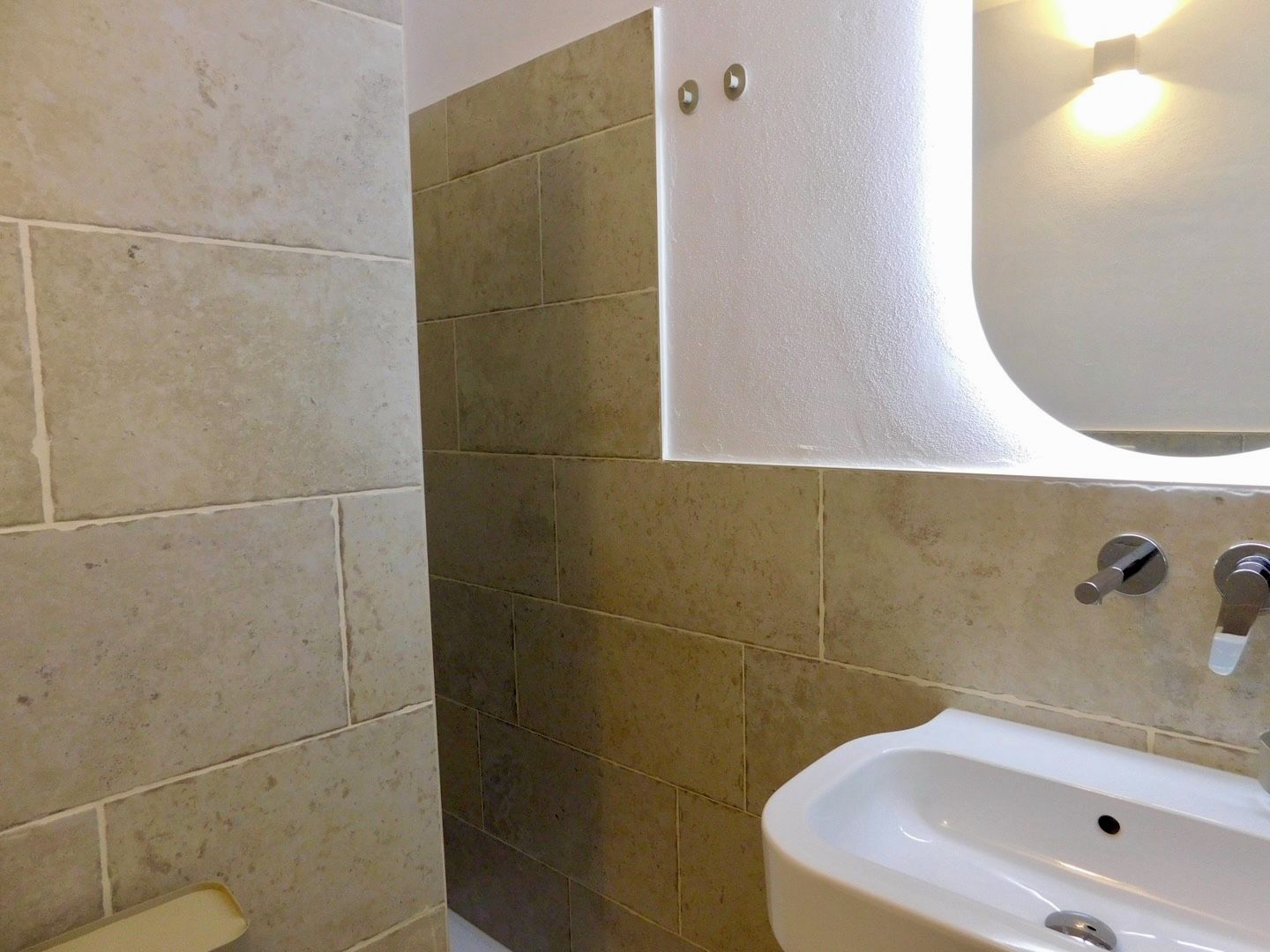 Ein Badezimmer mit einem weißen Waschbecken, einem Spiegel und beigen Fliesen.