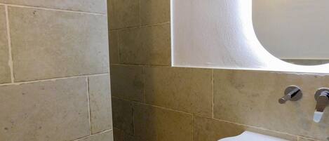 A bathroom with a white sink, a mirror, and beige tiles.