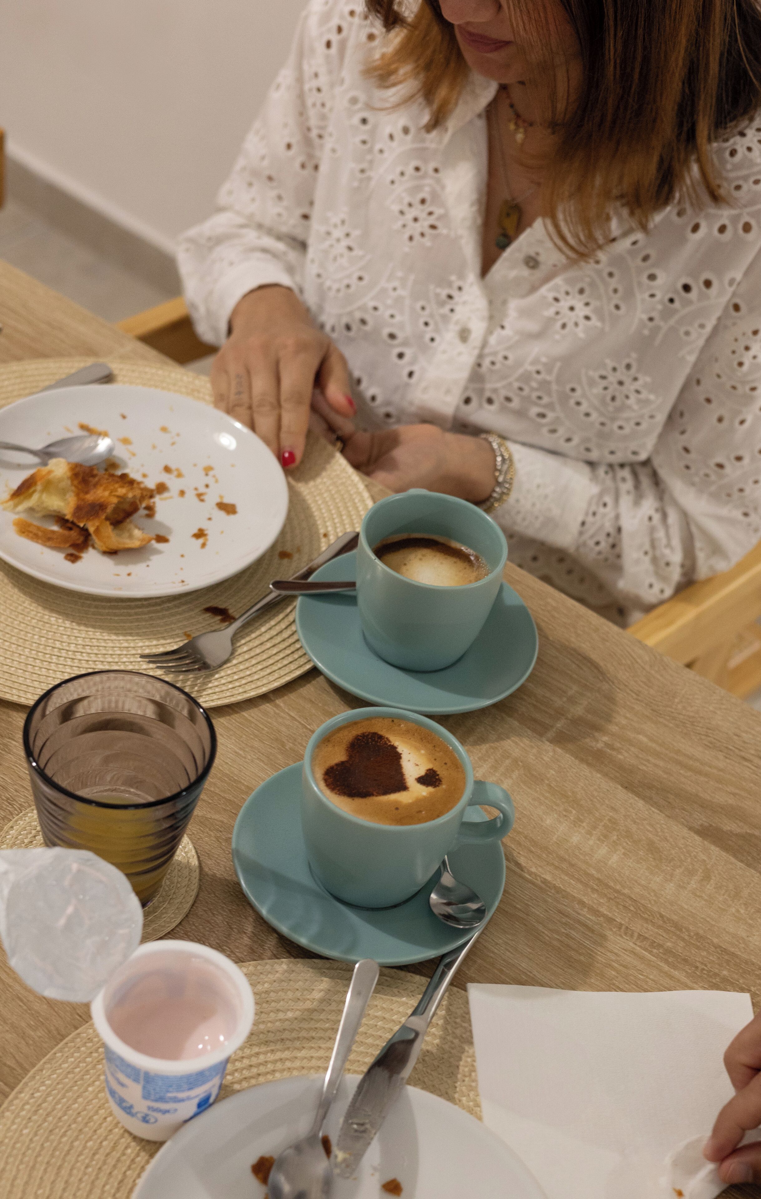 Ein Tisch mit einem Teller Essen, zwei Kaffeetassen, einem Glas Wasser und einem Joghurtbecher.