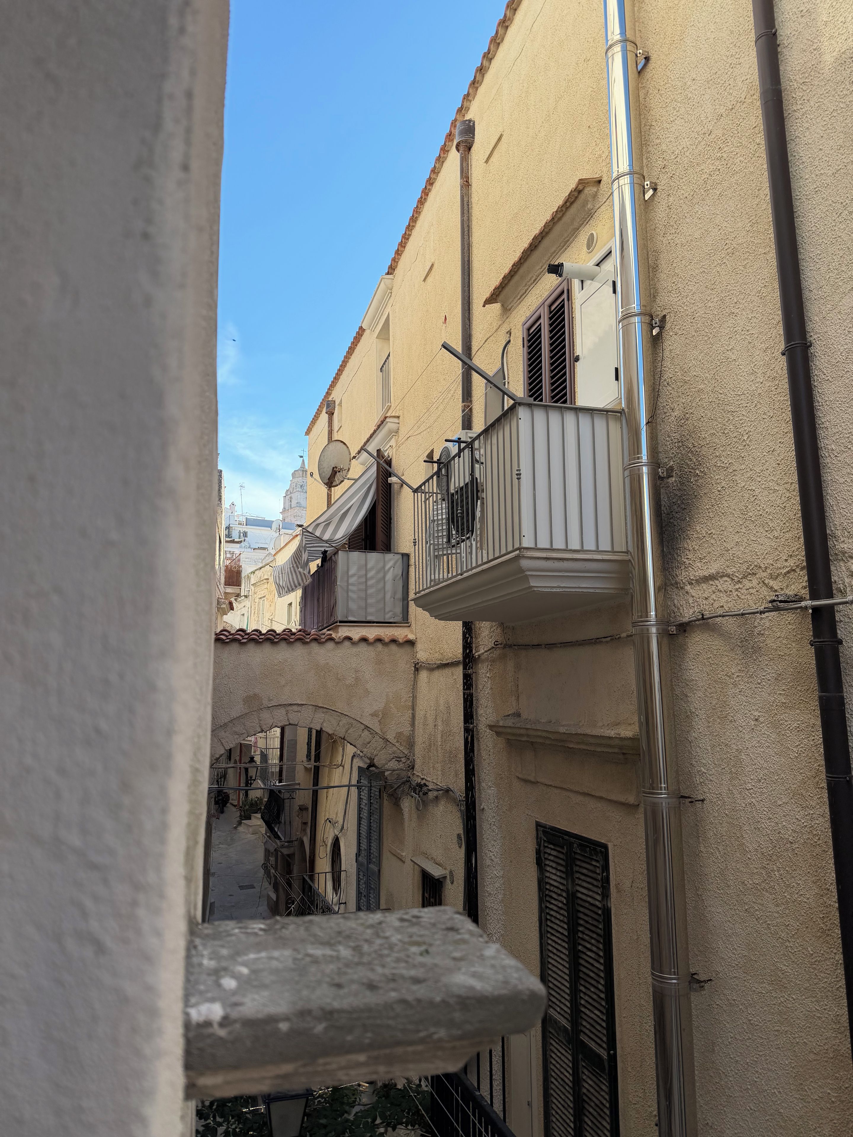 A narrow alleyway with buildings on either side, featuring balconies with railings and air conditioning units.