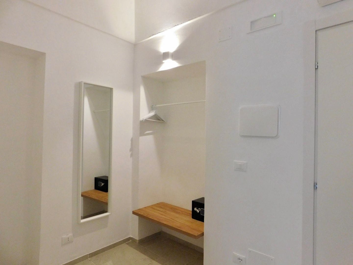 Un passadís amb un mirall, una prestatgeria de fusta i una porta.
