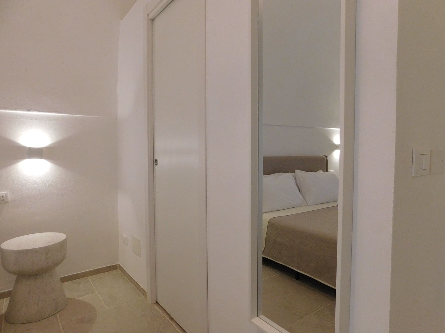 A bathroom with a toilet, a mirror, and a bed visible through the door.