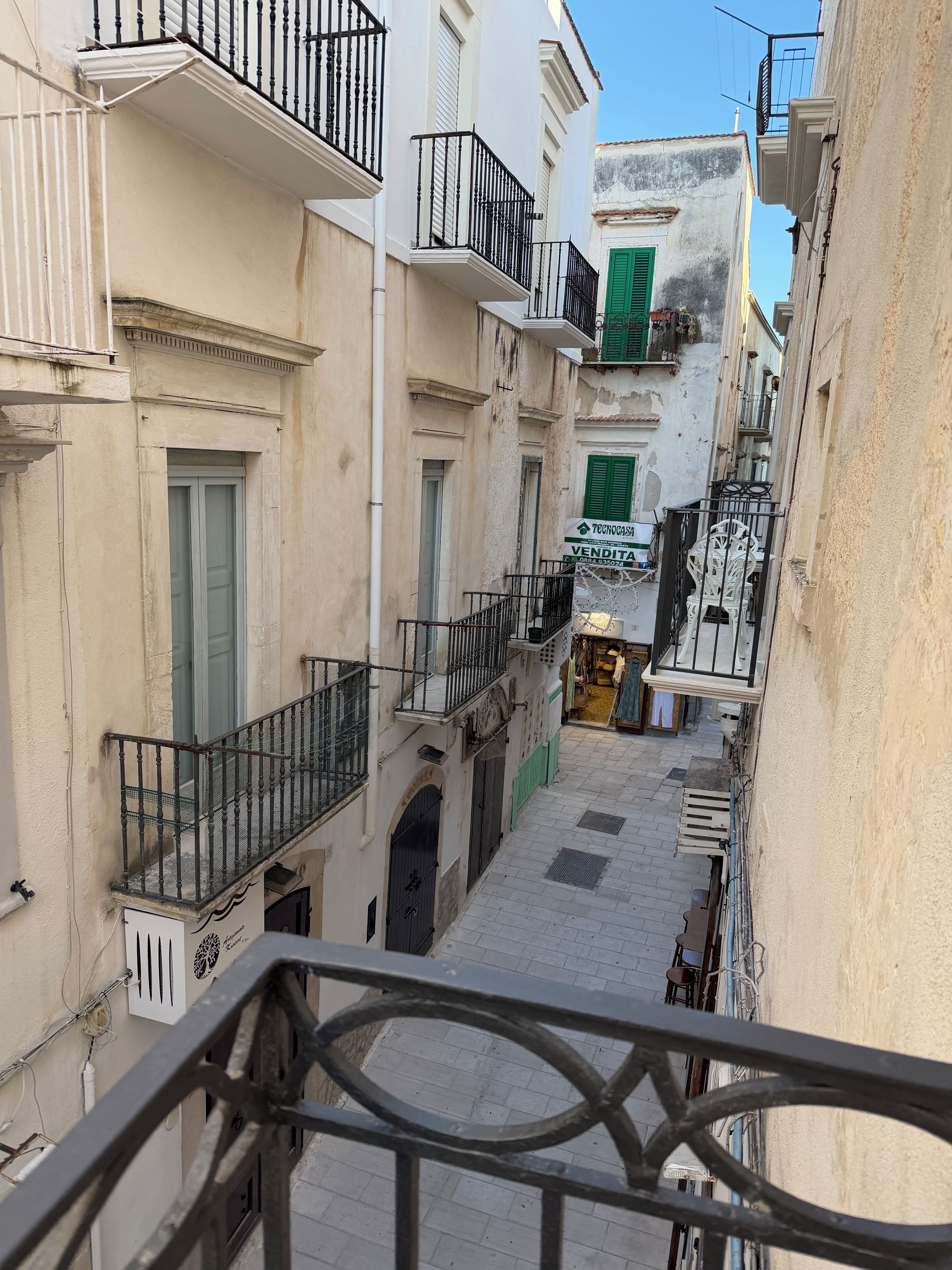 Una estrecha calle urbana con edificios que tienen balcones y una fachada comercial.