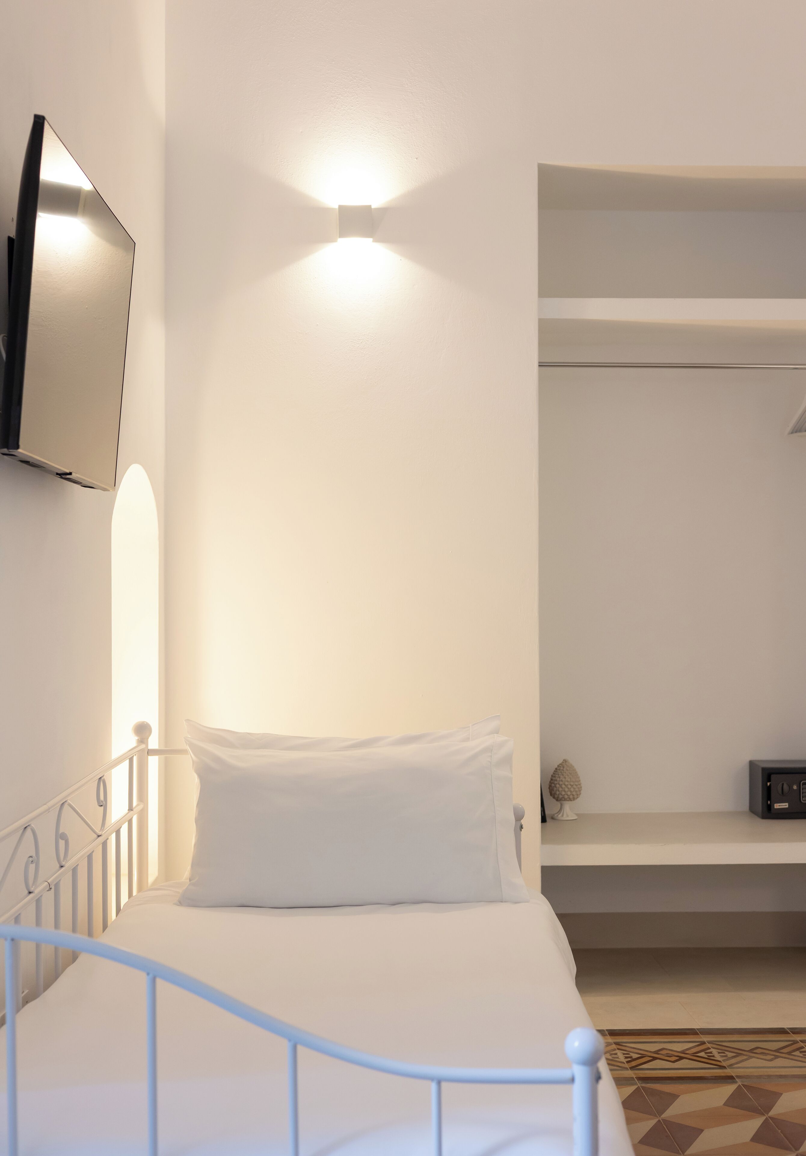 A bedroom with a bed, a TV mounted on the wall, and a shelf unit.
