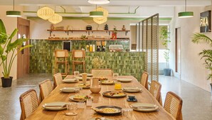 A dining area with a long wooden table, chairs, and hanging pendant lights. - Minimalist - The Varanasi Edit (Varanasi)