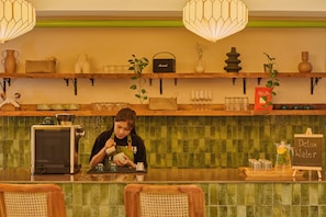 A barista preparing a drink at a counter with a coffee machine, shelves with various items, and a sign for detox water.