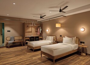 A modern hotel room with two beds, a desk, a wardrobe, and a ceiling fan.