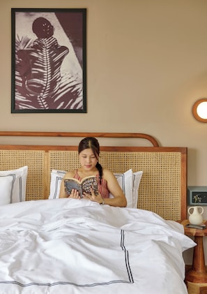 Una persona leyendo un libro en una cama con ropa blanca y un cabecero de ratán.