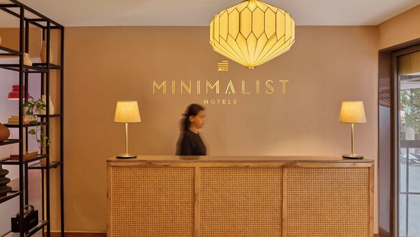 Ein Empfangstresen mit einem Schild, auf dem 'Minimalist Hotels' steht, eine geometrische Pendelleuchte und je eine Lampe auf beiden Seiten.