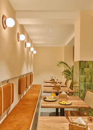 A restaurant with wooden tables, cushioned seating, and wall-mounted lights.
