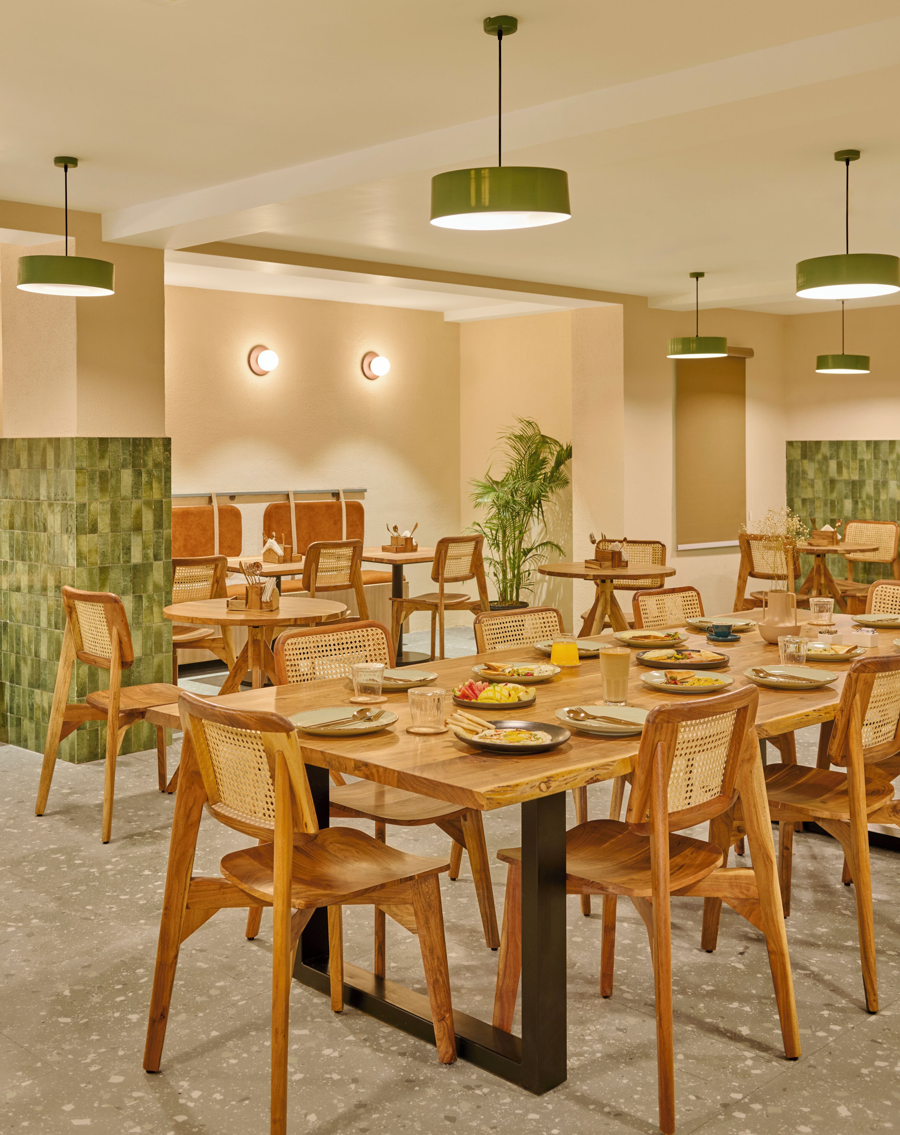 A dining area with round tables, wooden chairs, and green pendant lights.