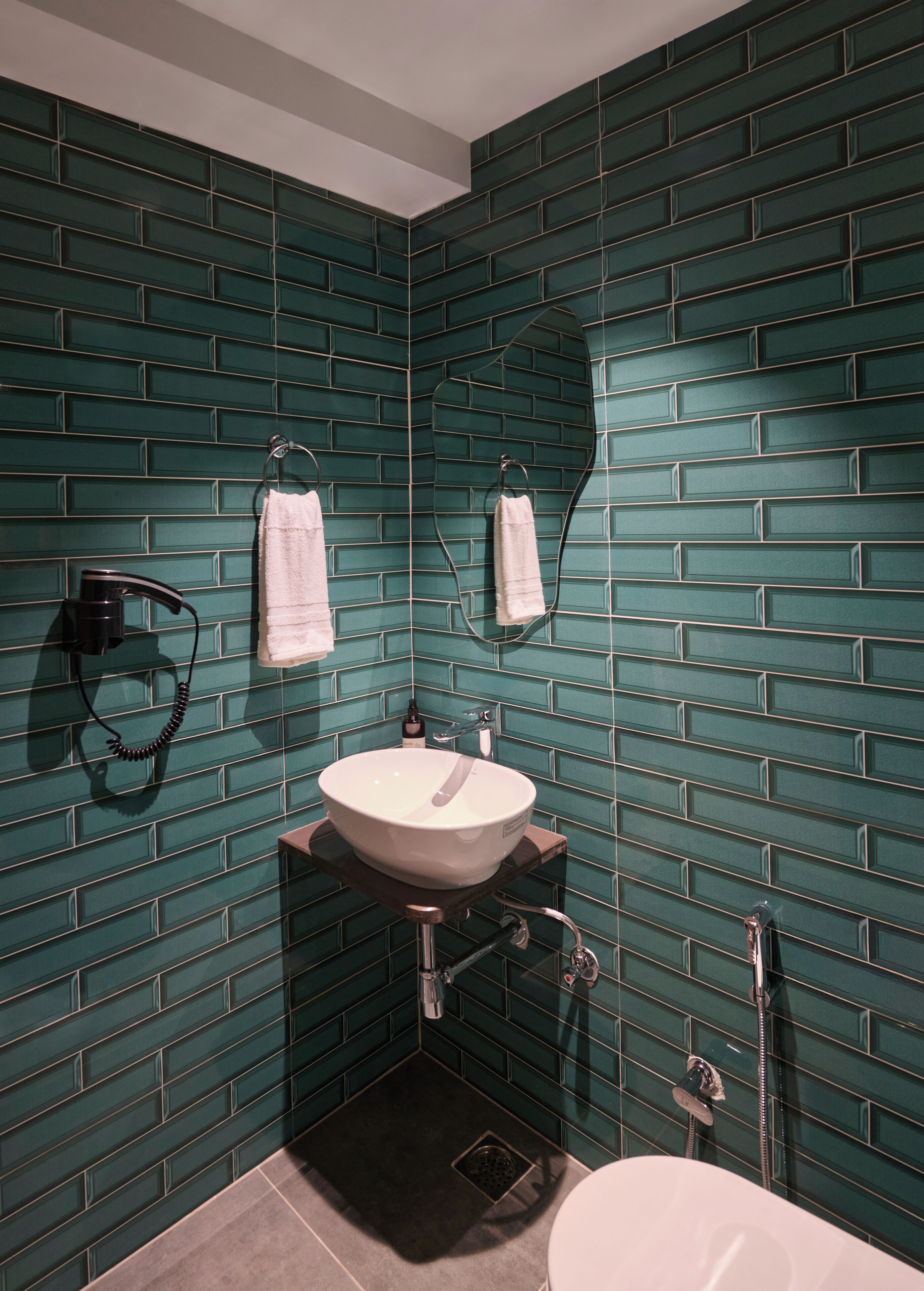 Ein Badezimmer mit grüner Fliesenwand, einem weißen Waschbecken, einem Handtuchhalter und einer Toilette.