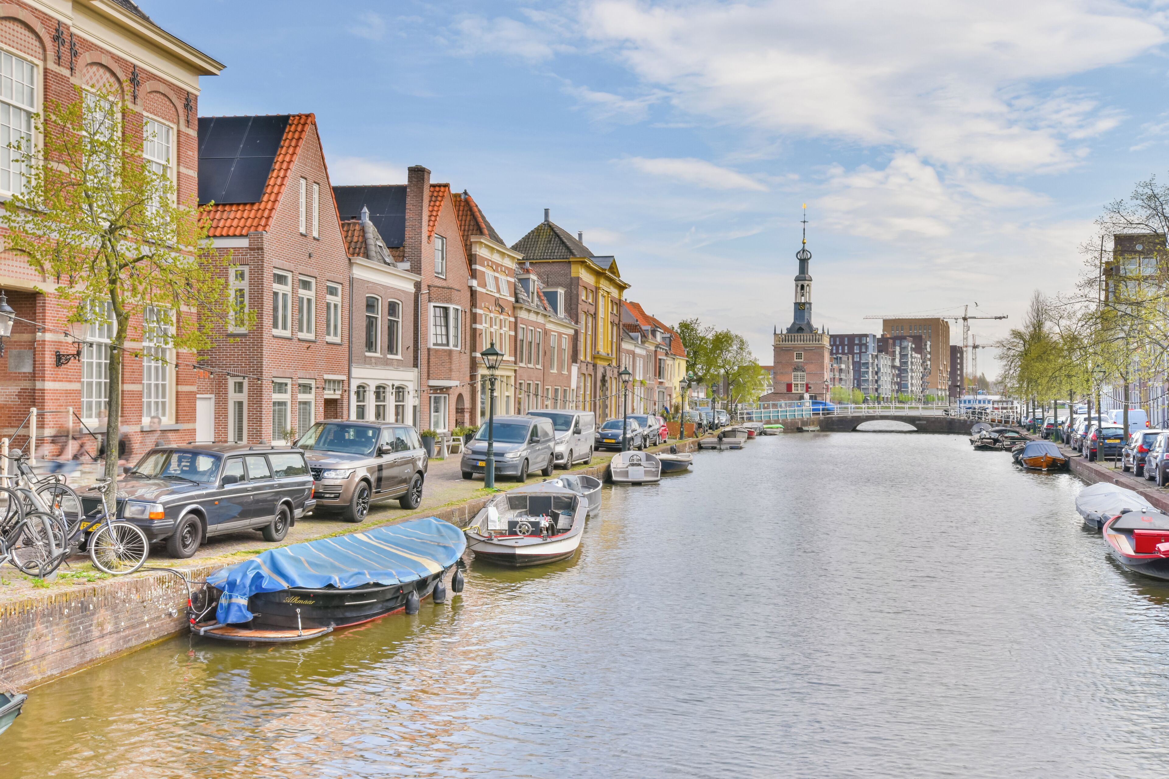 A canal with boats, parked cars, and historic buildings along the water.