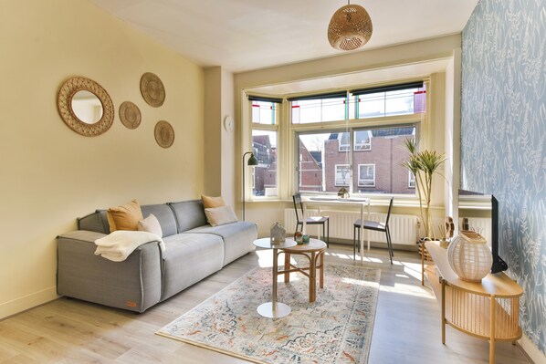 A modern living room with a grey sofa, a patterned rug, and a large window with a view of buildings.