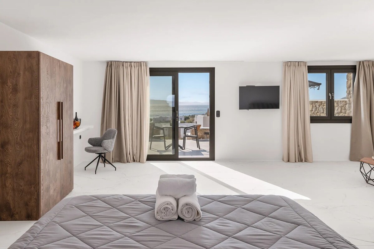 Un dormitorio moderno con cama, armario de madera, televisor y balcón con vistas.