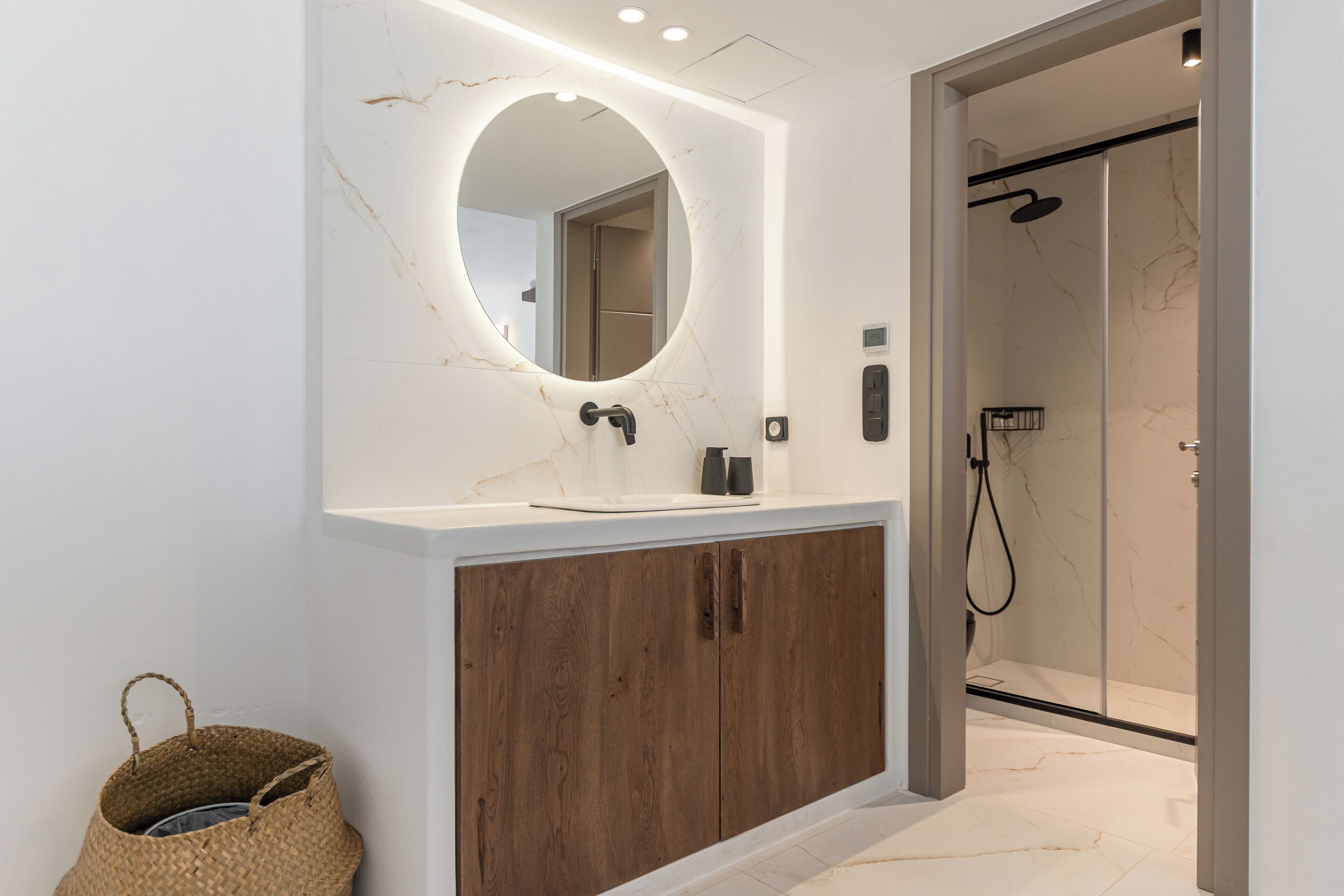 A modern bathroom with a marble vanity, wooden cabinet, and a glass-enclosed shower.