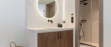 A modern bathroom with a marble vanity, wooden cabinet, and a glass-enclosed shower.