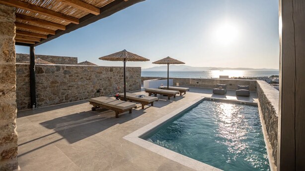 Un espace aménagé au bord de la piscine, avec des chaises longues et des parasols, offrant une vue sur une étendue d’eau et un paysage lointain.