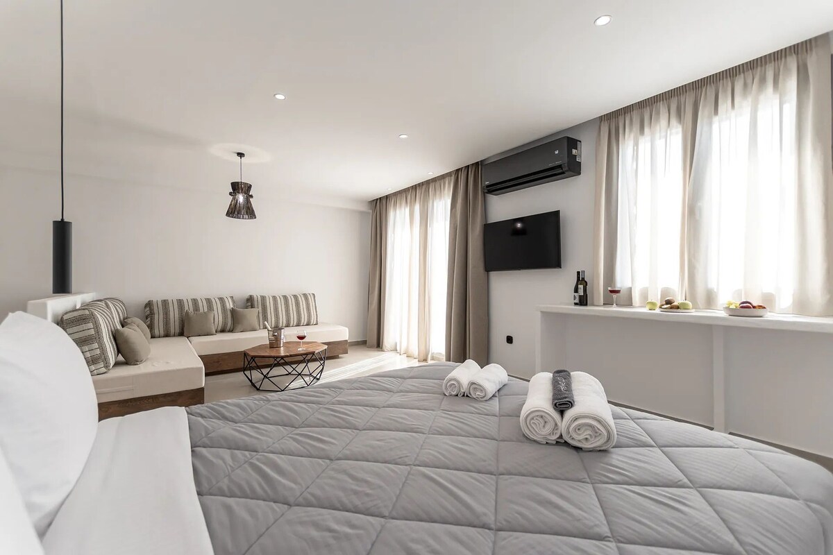 Quarto de hotel moderno com uma cama grande, um sofá, uma mesinha e uma televisão fixada na parede.