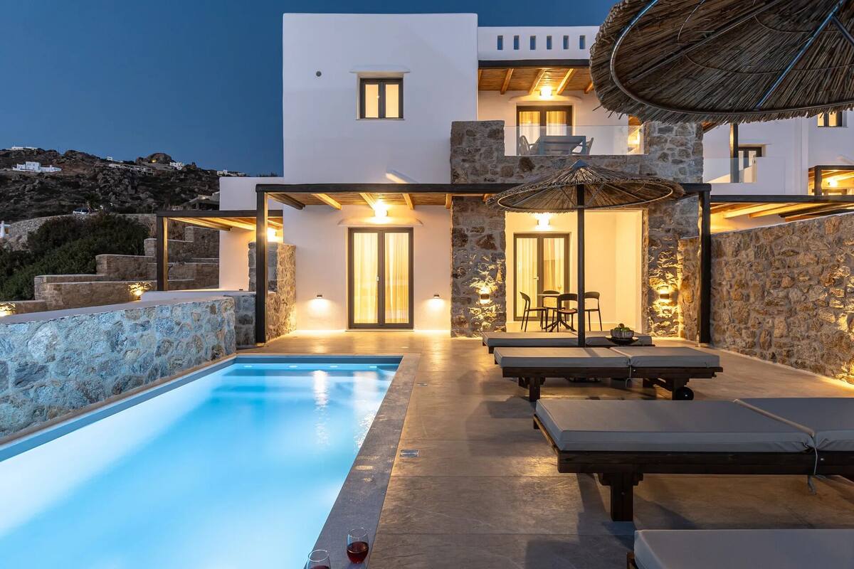 A modern villa with a swimming pool, stone walls, and outdoor seating.