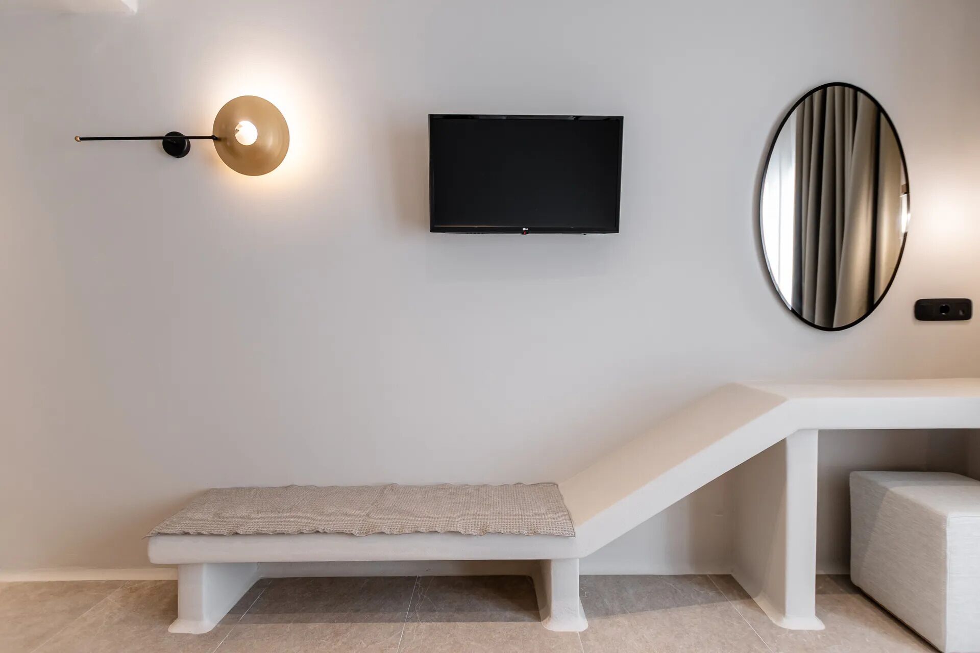 A modern room with a bench, a flat-screen TV, a wall-mounted light, and a mirror.