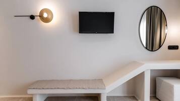 A modern room with a bench, a flat-screen TV, a wall-mounted light, and a mirror.