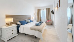 Een moderne slaapkamer met een groot bed, nachtkastjes, een leeslamp en een relax fauteuil.