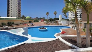 Een hotel met een groot zwembad, palmbomen en een helderblauwe lucht.
