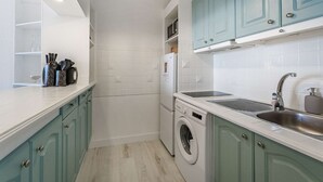Een kleine keuken met blauwgroene kastjes, een inbouw wasmachine en een gootsteen.