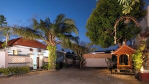 A courtyard with a tiled floor, palm trees, and a gazebo. - Kemala Living Sanur (Denpasar)