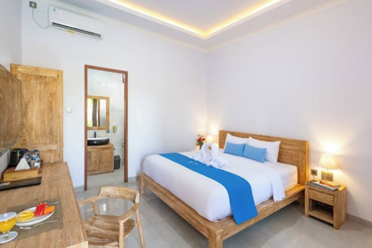 A hotel room with a wooden bed, bedside table, and a desk with a chair.