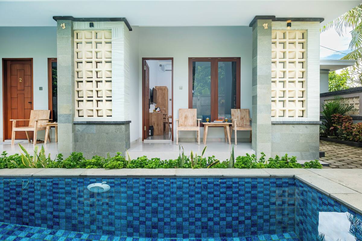 A poolside area with a tiled pool, wooden chairs, and a door marked with the number 2.