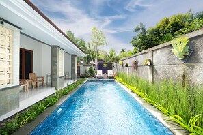 A swimming pool with a stone wall on one side and a white building on the other. - Kemala Living Sanur (Denpasar)