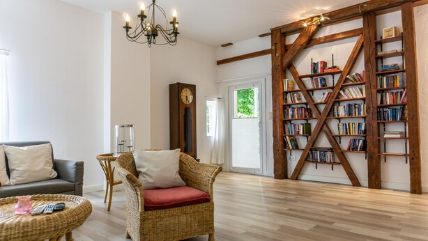 Ein Wohnzimmer mit Sofa, Korbsessel, Bücherregal und einer Chandelier.
