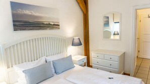 Ein Schlafzimmer mit Bett, Nachttisch, Kommode, Lampe, Spiegel und einem Bild an der Wand.