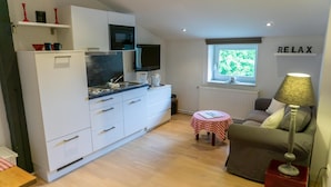 A compact living space with a kitchenette, a sofa, a small table, and a window with a view.