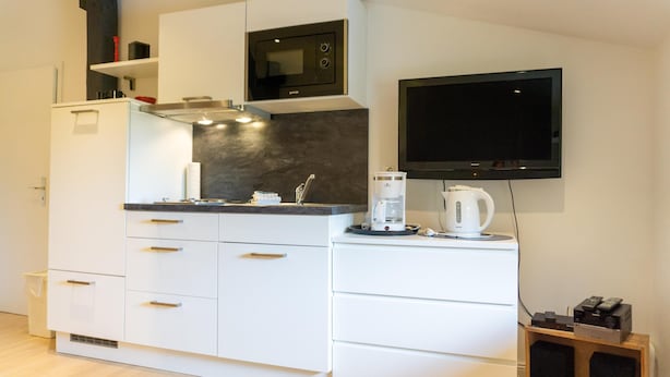 A modern kitchen with white cabinetry, a built-in microwave, a coffee maker, and a flat-screen TV mounted on the wall.