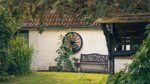 A rustic outdoor area with a white wall, a wooden bench, and a large wheel.