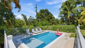 A rectangular swimming pool with a white fence, surrounded by palm trees and a clear sky. - Welcome to Your West Palm Beach Getaway! (West Palm Beach)