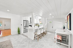Een moderne keuken met witte kastjes, een centraal eiland met barkrukken en een eethoek met een vloerkleed met patroon.