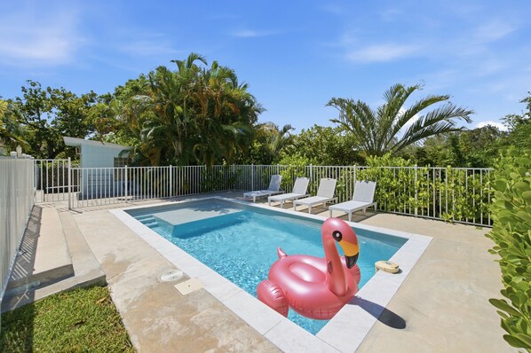 Una piscina con un flotador en forma de flamenco rosa, rodeada por una valla blanca y palmeras.