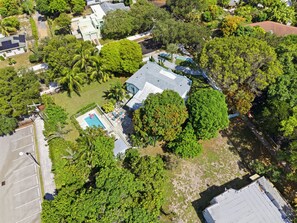 Vista aérea de una zona residencial con piscina, una casa de techo inclinado y abundante vegetación.