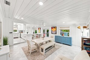 Una cocina amplia con muebles blancos, un comedor con una mesa grande y sillas, y un armario azul.